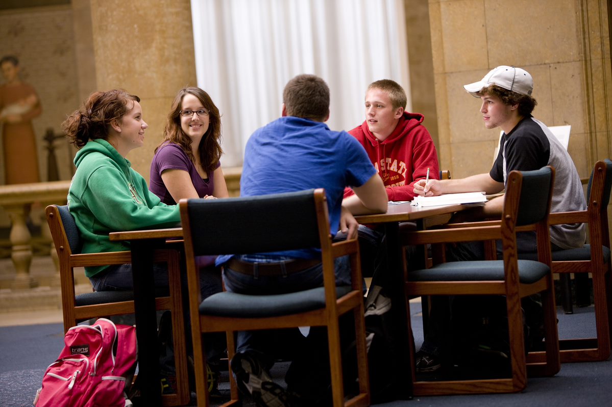 Five students around a table talking and studying